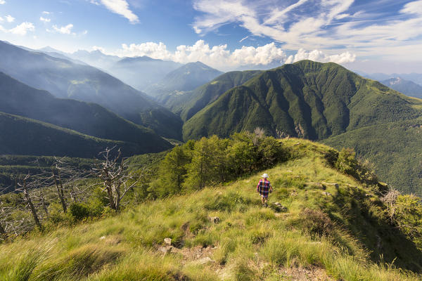 Hiker walks on Monte Legnoncino with Valvarrone and Valsassina in the background, Lecco province, Lombardy, Italy