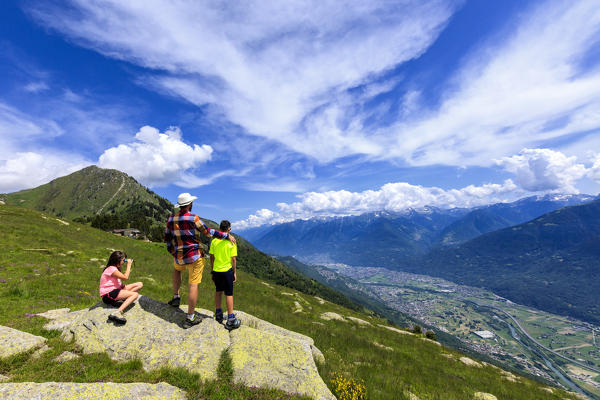 Father and sons enjoy the view towards Morbegno from Alpe Bassetta, Lower Valtellina, Sondrio province, Lombardy, Italy