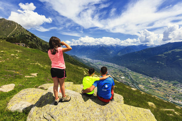 Father and sons look towards Morbegno from Alpe Bassetta, Lower Valtellina, Sondrio province, Lombardy, Italy