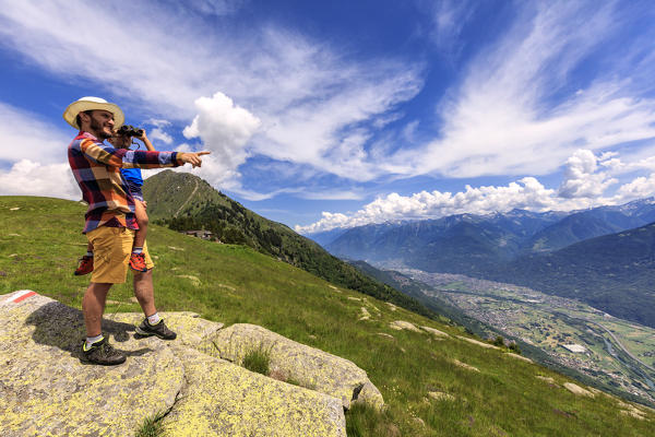 Little boy in father's arms looks to Morbegno with binoculars, Alpe Bassetta, Valtellina, Sondrio, Lombardy, Italy