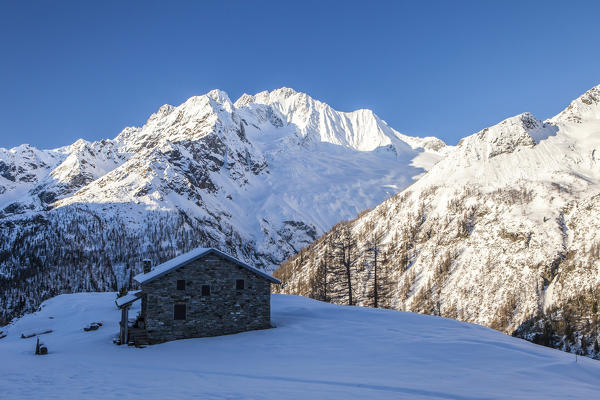 Stone hut at the foot of the snowy Monte Vazzeda, Alpe dell'Oro, Valmalenco, Valtellina, Sondrio province, Lombardy, Italy