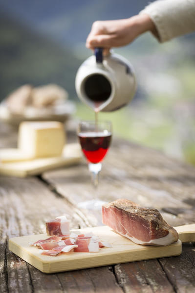 a piece of bacon (speck) with a hand filling a glass of wine, Bolzano province, South Tyrol, Trentino Alto Adige, Italy,