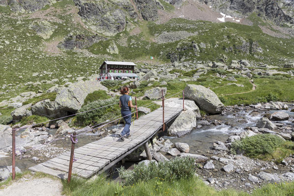 A trekker crosses a small wooden bridge to the Zamboni Zappa refuge at the foot of the East face of Monte Rosa Massif (Macugnaga, Anzasca Valley, Verbano Cusio Ossola province, Piedmont, Italy, Europe)