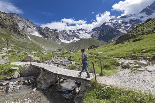 A trekker crosses a small wooden bridge near the Zamboni Zappa refuge at the foot of the East face of Monte Rosa Massif (Macugnaga, Anzasca Valley, Verbano Cusio Ossola province, Piedmont, Italy, Europe)