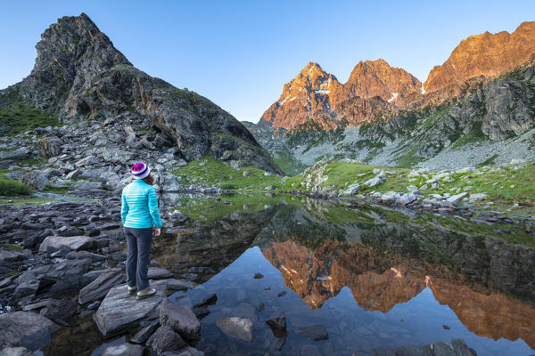 A girl is watching the Monviso Peak, reflected in a small alpine lake at sunrise (Fiorenza Lake, Pian del Re, Monviso Natural Park, Po Valley, Crissolo, Cuneo province, Piedmont, Italy, Europe) (MR)
