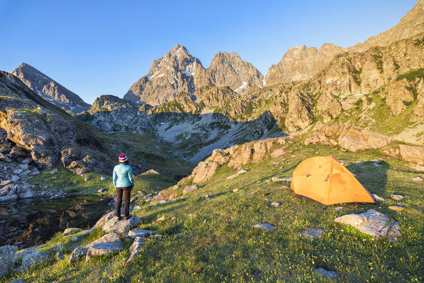 A girl is watching the Monviso Peak outside her tent at sunrise (Fiorenza Lake, Pian del Re, Monviso Natural Park, Po Valley, Crissolo, Cuneo province, Piedmont, Italy, Europe) (MR)