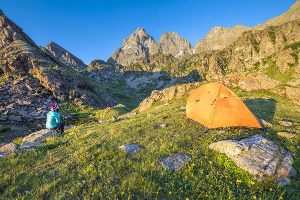 A girl is watching the Monviso Peak outside her tent at sunrise (Fiorenza Lake, Pian del Re, Monviso Natural Park, Po Valley, Crissolo, Cuneo province, Piedmont, Italy, Europe) (MR)