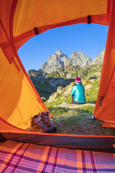 A girl is watching the Monviso Peak outside her tent (Fiorenza Lake, Pian del Re, Monviso Natural Park, Po Valley, Crissolo, Cuneo province, Piedmont, Italy, Europe)  (MR)