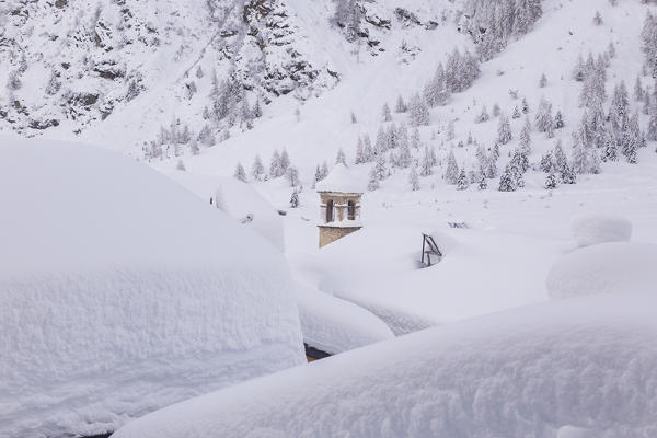 Bell tower of San Bernardo alpine church between snowcapped huts. Rezzalo valley, SOndalo, Sondrio district, Valtellina, Alps, Lombardy, Italy, Europe.