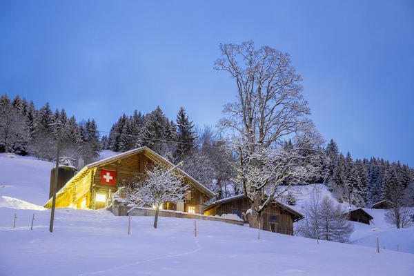 Traditional farm with switzerland flag at dusk. Grindelwald, Canton of Bern, Switzerland, Europe.