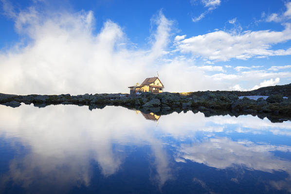 Benigni Refuge is reflected with fog in the water. Val Brembana, Lombardy, Italy, Europe.