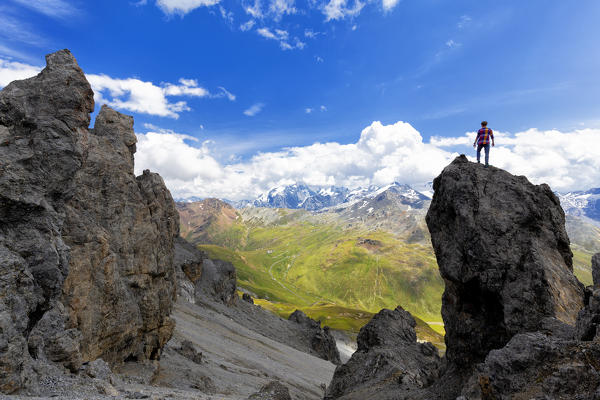 A boy looks the street of Passo dello Stelvio from a rock pinnacle. Passo dello Stelvio, National Park of Stelvio, Valtellina, Lombardy, Italy, Europe.