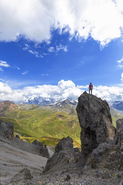 A boy looks the street of Passo dello Stelvio from a rock pinnacle. Passo dello Stelvio, National Park of Stelvio, Valtellina, Lombardy, Italy, Europe.