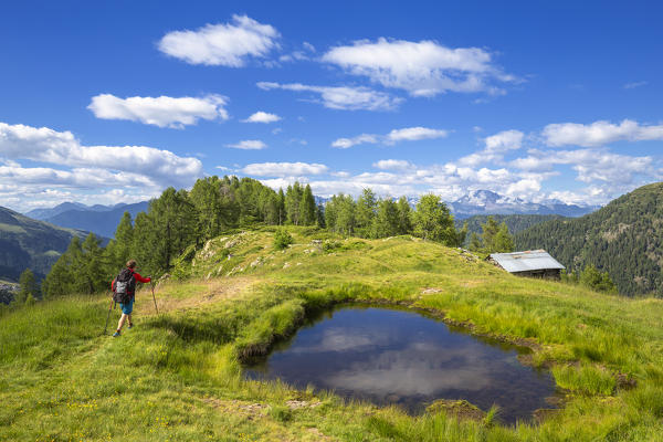 Hiker walks near a hut with alpine pond. Valgerola, Orobie Alps, Valtellina, Lombardy, Italy, Europe