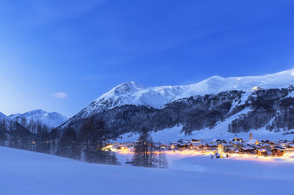 Village illuminated during twilight. Livigno, Valtellina, Lombardy, Italy, Europe.