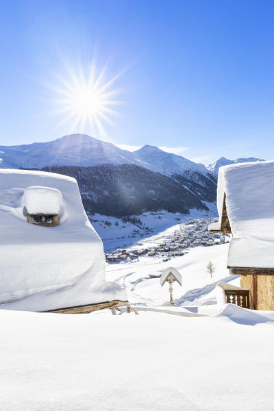 Snow covered roofs after a snowfall with sun in the background. Livigno, Valtellina, Lombardy, Italy, Europe.