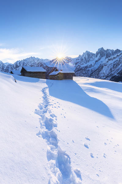 Footprint in the fresh snow with traditional huts in the background. Soglio, Bregaglia Valley, Canton of Grisons, Switzerland, Europe.