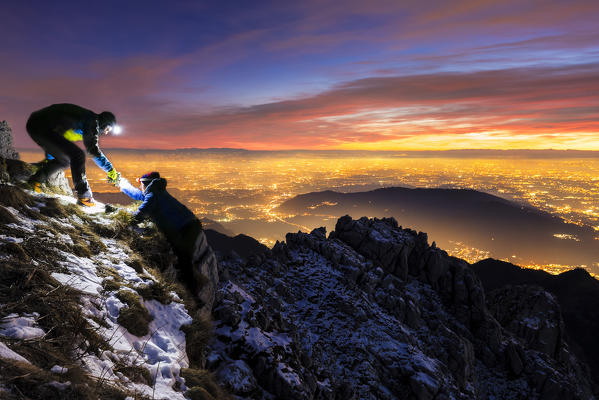 A hiker helps another person to climb the mountain at night. Mount Resegone, Lombardy, Italy, Europe.