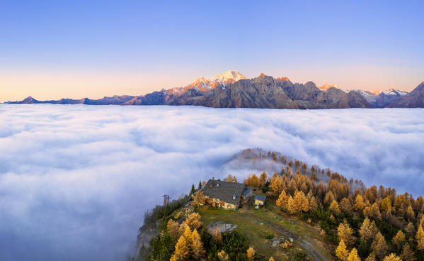 Fog covers the Valmalenco(Val Malenco) with the mountain range of Disgrazia illuminated by sunrise in the background and the Motta mountain hut in the foreground. Valtellina, Lombardy, Italy, Europe.