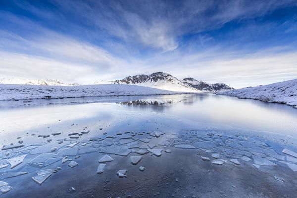 Clouds is reflected in the icy surface of alpine lake. Stelvio pass, Valtellina, Lombardy, Italy, Europe.