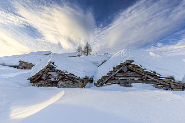 Stunning clouds at sunrise above traditional old huts in winter. Valmalenco, Valtellina, Lombardy, Italy, Europe.