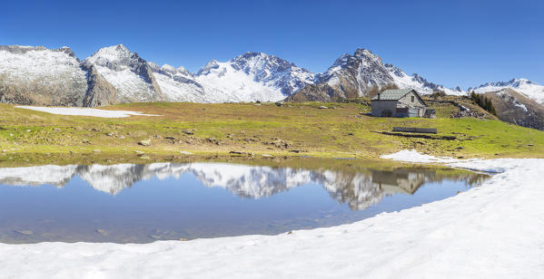 Panoramic view of traditional hut and group of Disgrazia is refected in a small lake. Valtellina, Sondrio province, Lombardy, Italy, Europe.