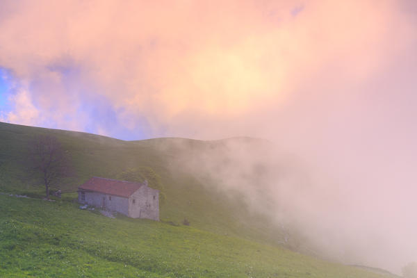 Old house with colorful clouds during sunset. Monte Linzone, Valico di Valcava(Valcava Pass), Val San Martino, Prealpi Bergamasche, Bergamo province, Lombardy, Italy.