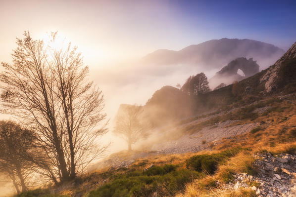 The sun illuminates the fog with the Porta di Prada in the background. Bocchetta di Prada, Grigna Settentrionale(Grignone), Northern Grigna Regional Park, Lombardy, Italy, Europe.