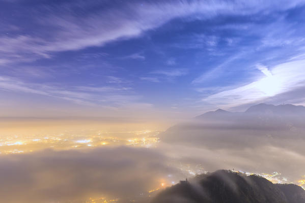 Moon hidden by clouds, illuminates the fog above the Brianza. Monte Barro Regional Park, Brianza, Lombardy, Italy, Europe.