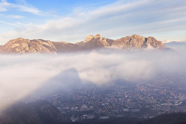 Monte Barro casts its shadow on the fog illuminates by sun, with Corni di Canzo group in the background. Monte Barro Regional Park, Brianza, Lombardy, Italy, Europe.