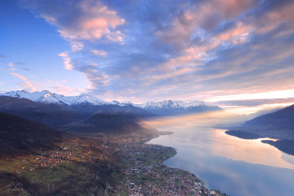 A ray of sun illuminates the village of Stazzona at sunrise. San Bernardo Church, Monte Bregagno, Dongo, Como Lake, Lombardy, Italy, Europe.