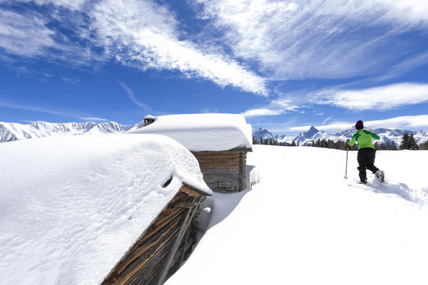 A trekker walks in the fresh snow with snowshoes near typical alpine huts. Wiesner Alp, Davos Wiesen, Landwasser Valley, Albula Valley, District of Prattigau/Davos, Canton of Graubünden, Switzerland, Europe.