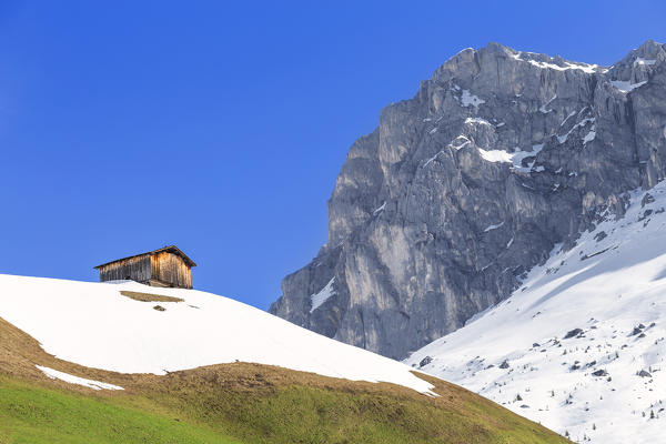 Typical hut during spring thaw in Partnun with Ratikon mountain range in the background. Partnun, Prattigau valley, District of Prattigau/Davos, Canton of Graubünden, Switzerland, Europe.