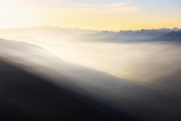 The valley covered by morning fog at sunrise. Valtellina, Lombardy, Italy, Europe.