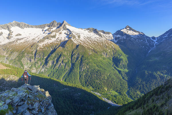 A hiker looks the valley from above. Torrione Pirola, Chiareggio valley, Valmalenco, Valtellina, Lombardy, Italy, Europe.