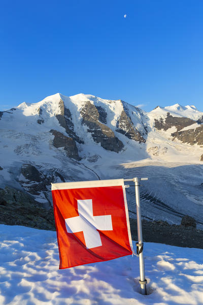 Switzerland flag with Palù Peaks and Vedret Pers Glacier in the background. Diavolezza Refuge, Bernina Pass, Engadin, Graubünden, Switzerland, Europe.