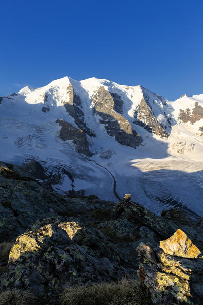 First sunlight illuminates rocks with Palù Peaks and Vedret Pers Glacier in the background. Diavolezza Refuge, Bernina Pass, Engadin, Graubünden, Switzerland, Europe.