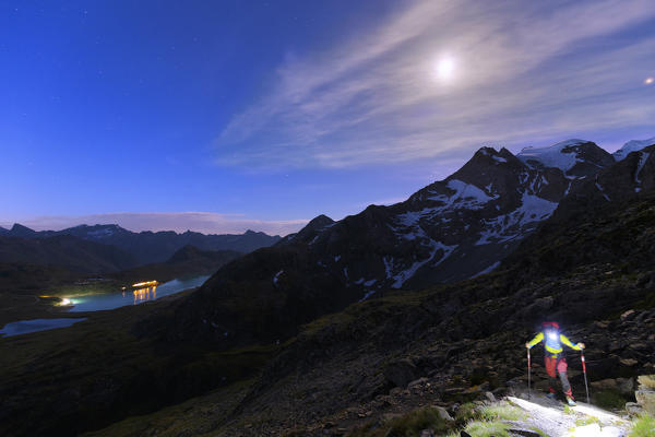 Hiker walks in the night of full moon with view on Bernina Pass, Engadin, Graubünden, Switzerland, Europe.