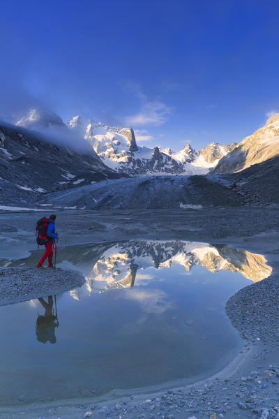 Hikers looks sunrise from a pond at Forno Glacier, Forno Valley, Maloja Pass, Engadin, Graubünden, Switzerland, Europe.