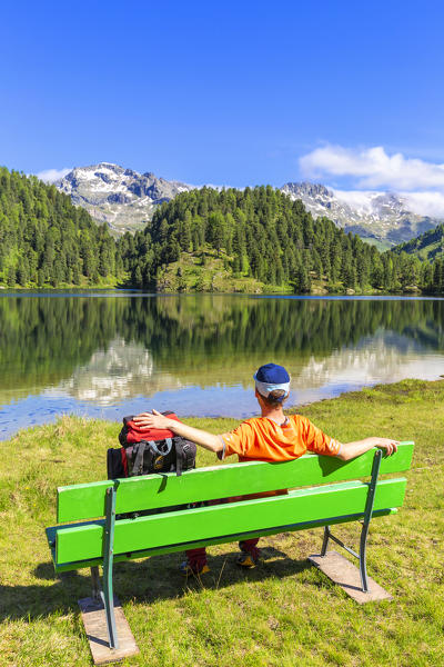 Hikers with backpack relaxes on a bench. Lake Cavloc, Lake Cavloc, Forno Valley, Maloja Pass, Engadin, Graubünden, Switzerland, Europe. (MR)