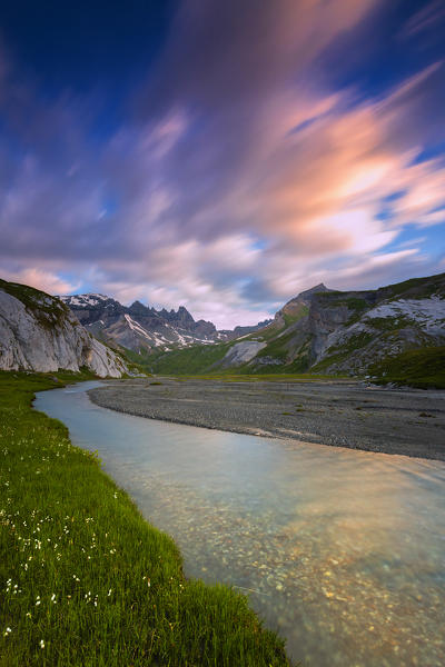 Clouds are reflected in the stream during a windy sunrise. Unterer Segnesboden, Flims, District of Imboden, Canton of Grisons, Switzerland, Europe