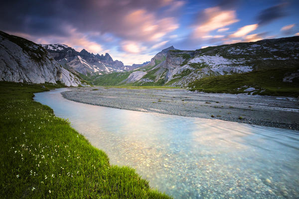 Clouds are reflected in the stream during a windy sunrise. Unterer Segnesboden, Flims, District of Imboden, Canton of Grisons, Switzerland, Europe