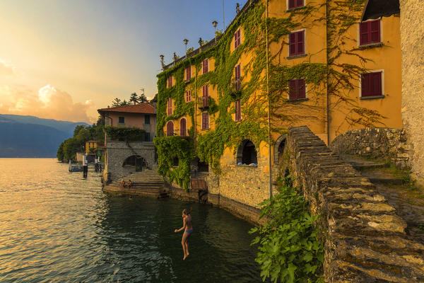 Girl dives into the lake from a bridge during sunset. Nesso, Province of Como,  Como Lake, Lombardy, Italy, Europe.