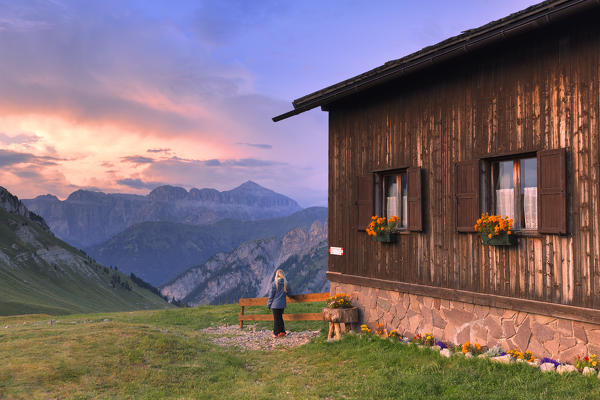 Girl looks sunset at Passo San Nicolò Refuge, San Nicolò Pass, Fassa Valley, Trentino, Dolomites, Italy, Europe.