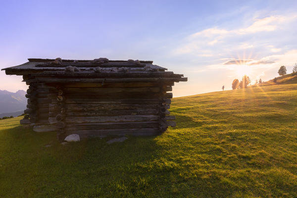 Traditional hut with one person that walks towards the sun. Gardena Valley, South Tyrol, Dolomites, Italy, Europe.