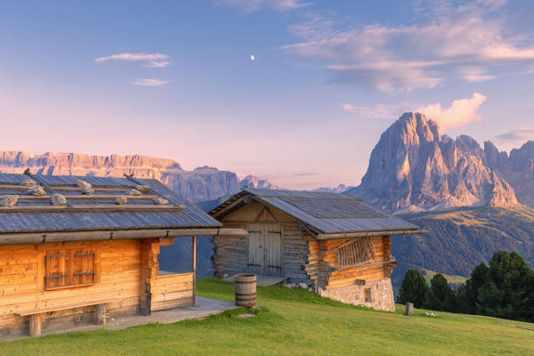 Traditional huts at sunset with Sassolungo and Sella Group in the background. Gardena Valley, South Tyrol, Dolomites, Italy, Europe.