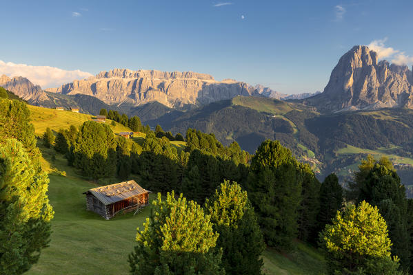 Last rays of sun on traditional hut with view on Sassolungo and Sella Group. Gardena Valley, South Tyrol, Dolomites, Italy, Europe.