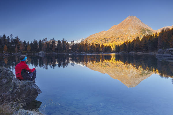 Hiker take a break to admire sunrise on lake Saoseo and Corn da Murasciola mount, Poschiavo, val di Campo, Canton of Graubunden, Switzerland, Europe (MR)
