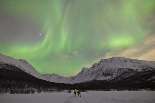 two people enjoy the spectacle of the northen lights during a cold winter night, Troms, Norway, Europe