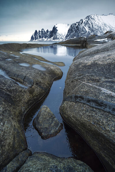 a large pool of water reflects the Devil's teeth mount during a winter day, Senja, Norway, Europe